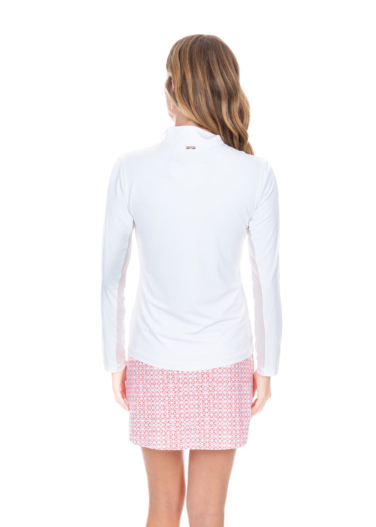 A blonde woman turned around wearing the Algarve Skort with a matching White 1/4 Zip Sport Top in front of a white background.
