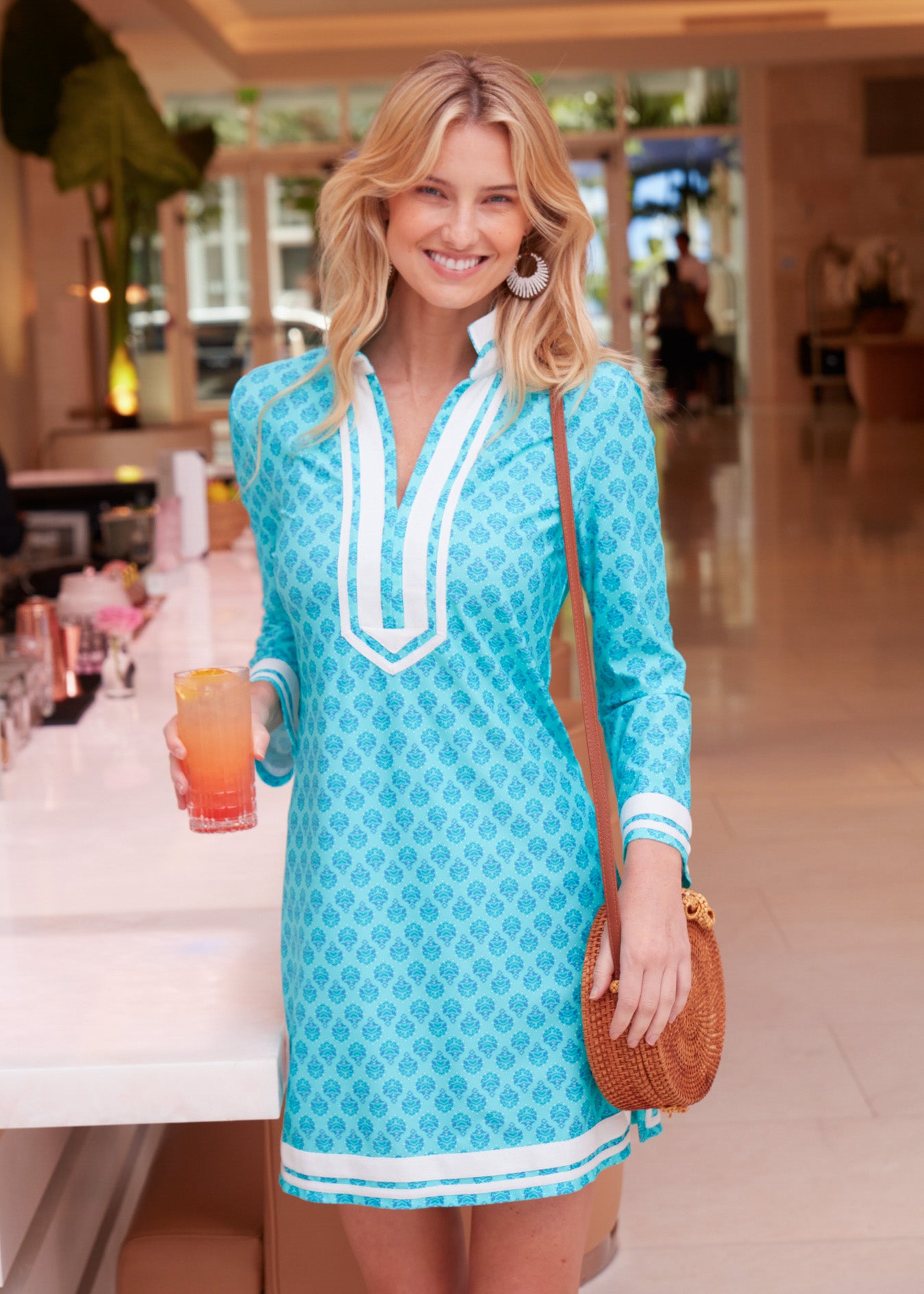 Blonde woman wearing Amalfi Coast Tunic Dress holding drink in hand and with purse on shoulder.