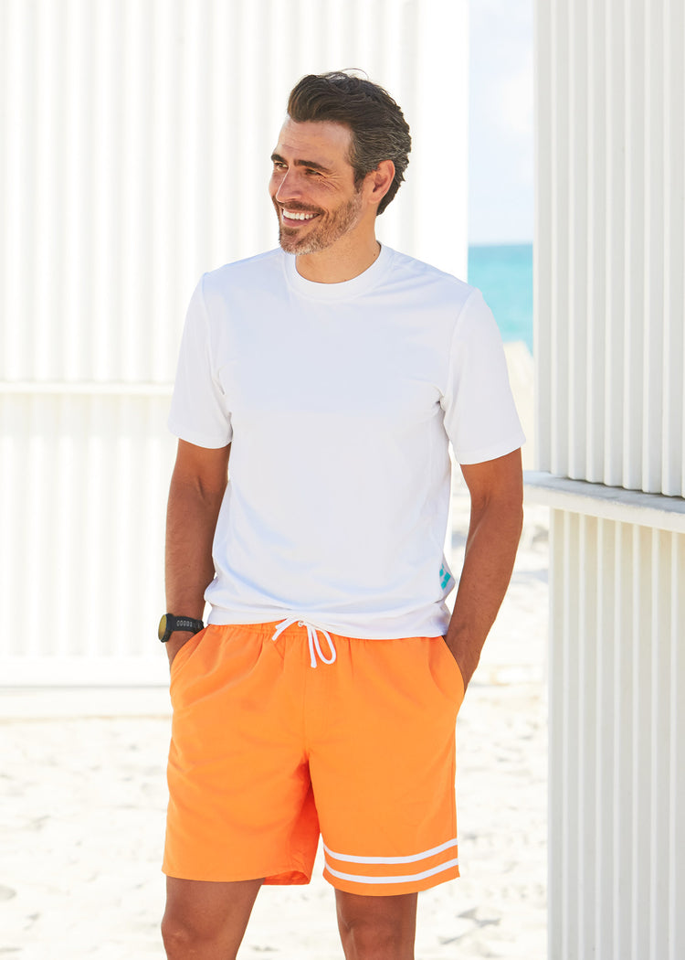 Man walking on beach wearing Cabana Life White Short Sleeve Rashguard with Tangerine Swim Trunks