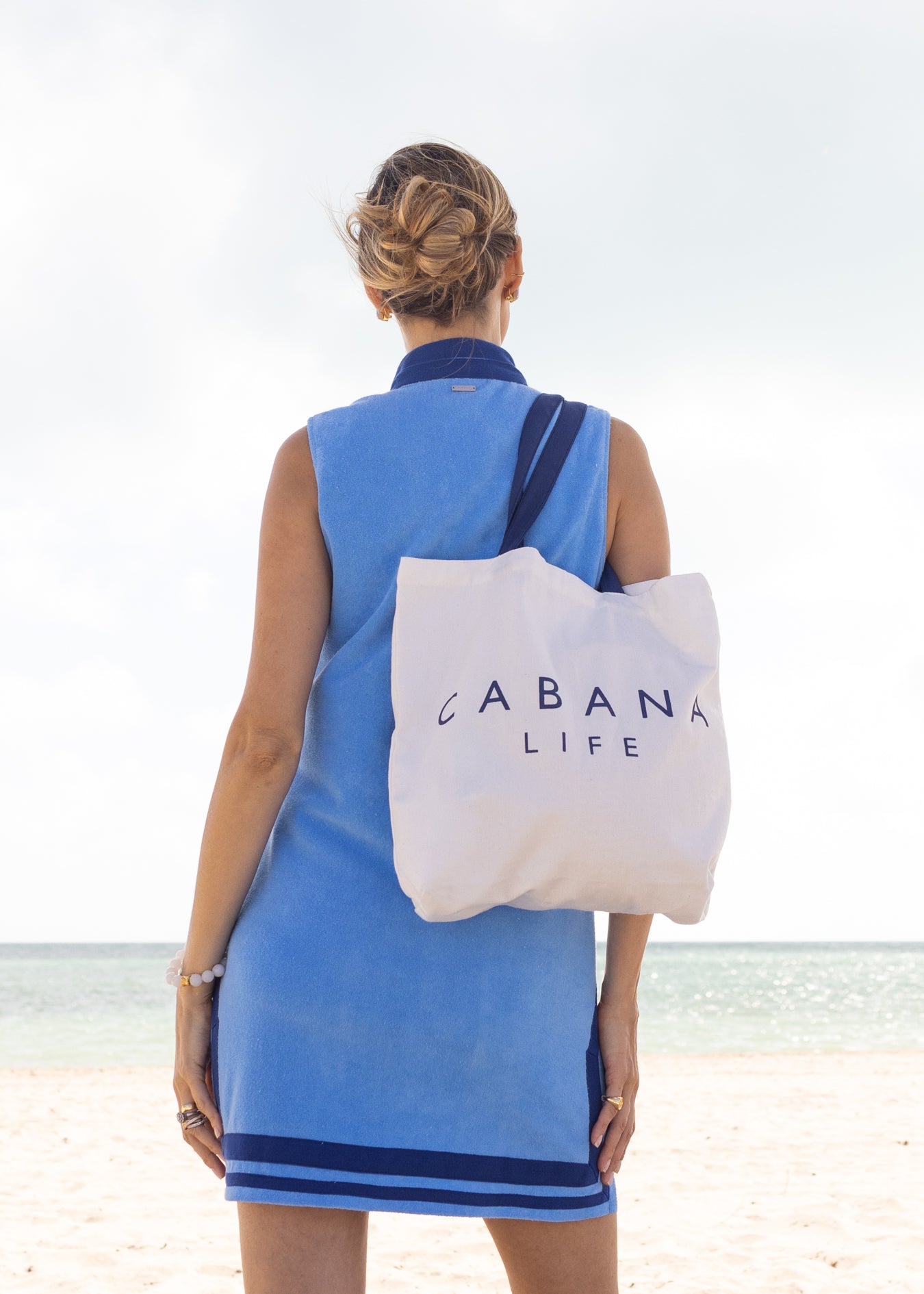 Woman wearing Blue/Navy Trim Sleeveless Terry Tunic holding Cabana Life Tote Bag on beach